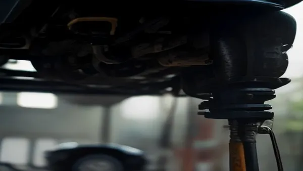 Mecânico inspecionando a suspensão dianteira de um carro elevado numa oficina